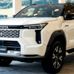 Front three-quarter view of the 2026 Toyota Fortuner GR-S top model in black color featuring sporty GR styling, LED headlights, large alloy wheels, muscular body design, and premium SUV stance on a highway road.